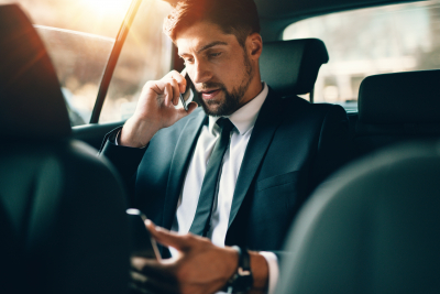 young businessman talking on mobile phone while sitting on back seat of a car.